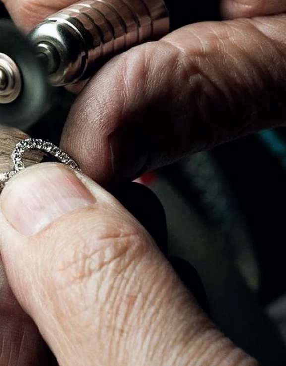 A jeweller fitting a diamond eternity band on a customer's finger with a sizing tool at the workbench