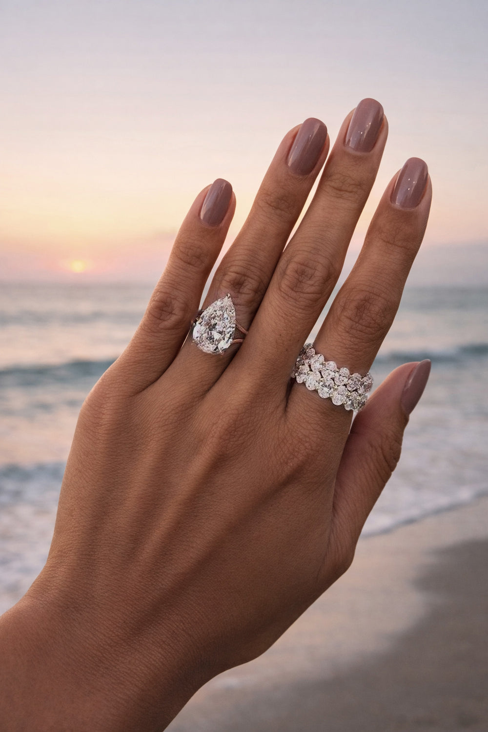 Hand at sunset wearing pear-cut diamond ring stacked with oval eternity bands